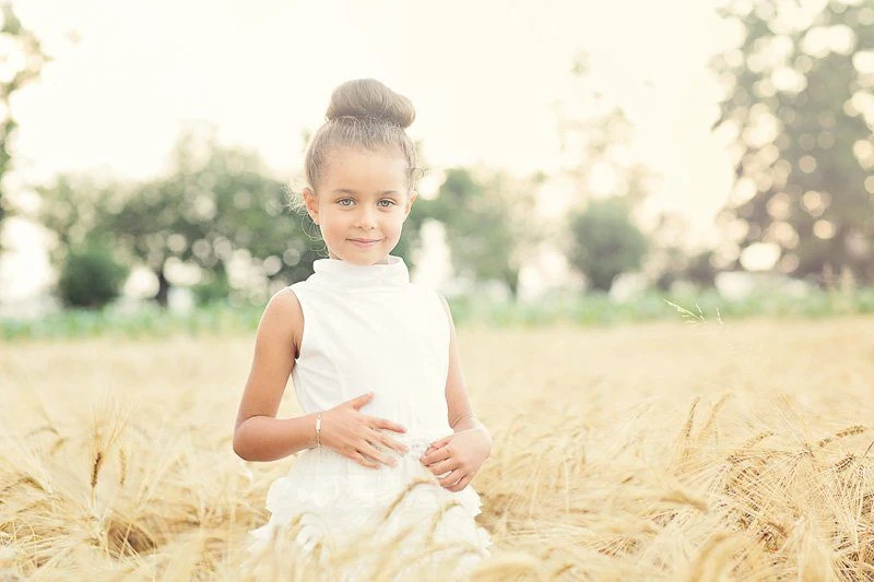 Bambina con le mani raccolte sul petto in un campo di grano
