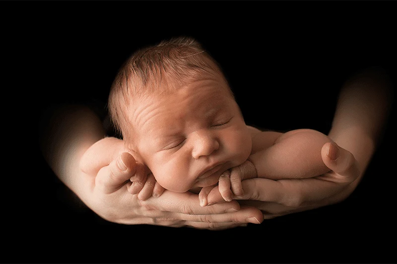 Neonato addormentato sostenuto dalle mani di un adulto