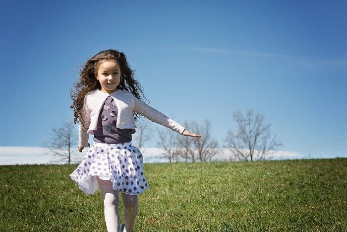 Bambina corre su un prato sotto il cielo azzurro