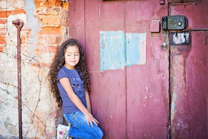 Bambina seduta davanti a una porta rossa