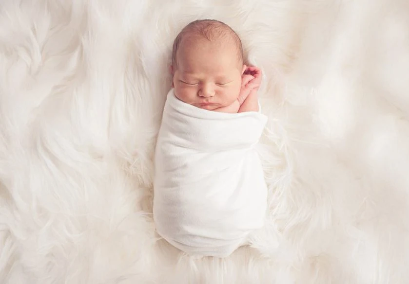 Neonato che dorme appoggiato su un morbido tappeto bianco